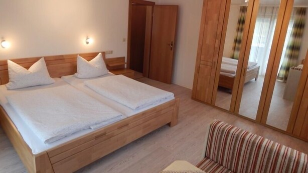 Een slaapkamer met een houten bed, een gestreepte bank en een kledingkast.