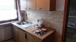 Een kleine keuken met houten kastjes, een spoelbak, een koffiezetapparaat en een kookplaat.