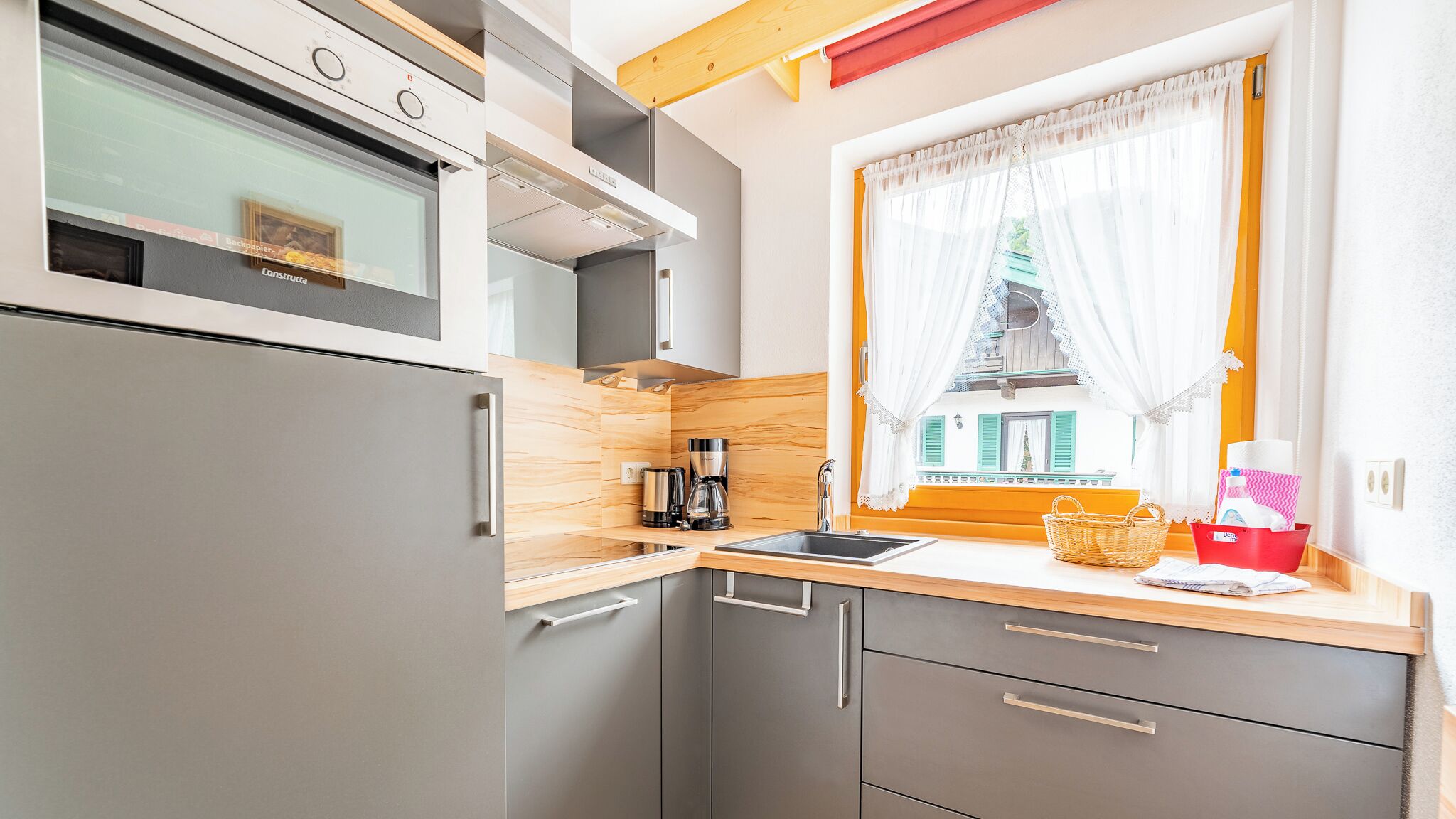 Eine kleine Küche mit integriertem Backofen, einer Kaffeemaschine und einem Fenster mit Vorhängen.