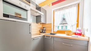 A compact kitchen with a built-in oven, a coffee maker, and a window with curtains.