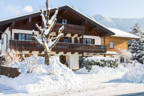 Un chalet en bois à deux étages, doté de balcons, entouré d’un paysage enneigé et d’arbres.