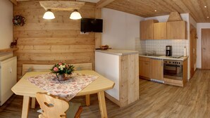 Um interior em madeira com uma mesa de jantar, cadeiras, uma TV e uma área de cozinha.