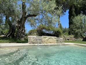 A clear pool surrounded by stone walls and large trees.