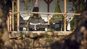 An outdoor seating area with wicker furniture and a table set for dining, surrounded by stone walls and shaded by a wooden pergola. - Le Balze Charming Apartment with private veranda, 10 min from Perugia Centre (Perugia)