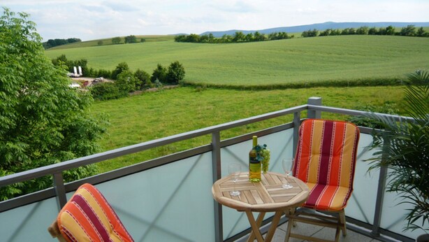 A balcony with two striped chairs and a small table, overlooking a green field. - APARTMENT II - PUMMPÄLZHOF (Bad Salzungen)