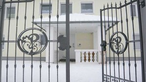 A gated entrance to a building with a snow-covered roof and a balcony with ornate railings.