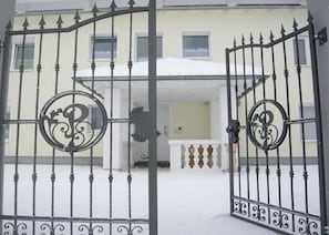 Una entrada protegida por un portón a un edificio con techo nevado y un balcón con barandilla ornamentada.
