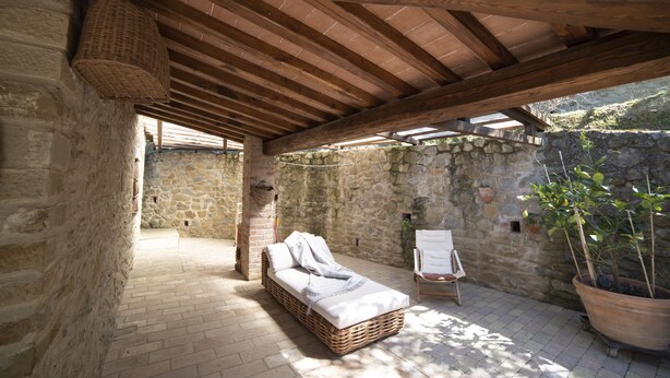 A rustic stone-walled room with a wicker bed, a wooden ceiling, and a potted plant.