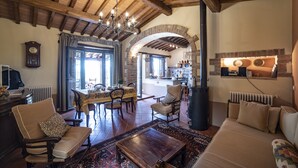 A spacious living room with a high wooden ceiling, a fireplace, and a dining area with a table and chairs.