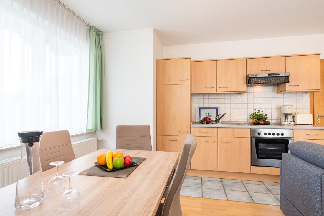 Een moderne keuken met houten kastjes, een ingebouwde oven en een eethoek met een tafel gedekt voor twee personen.