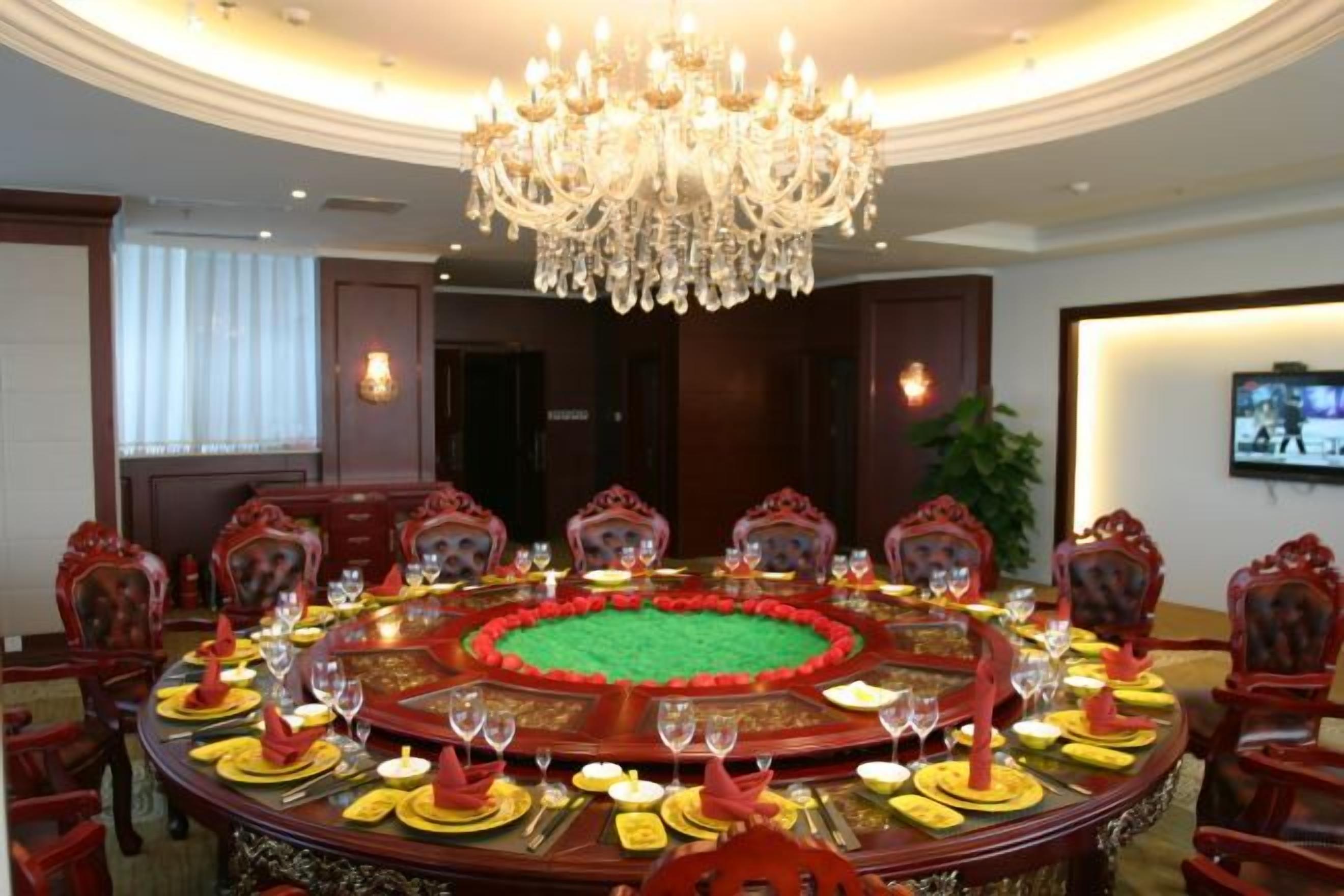 A formal dining room with a round table, red chairs, and a chandelier.
