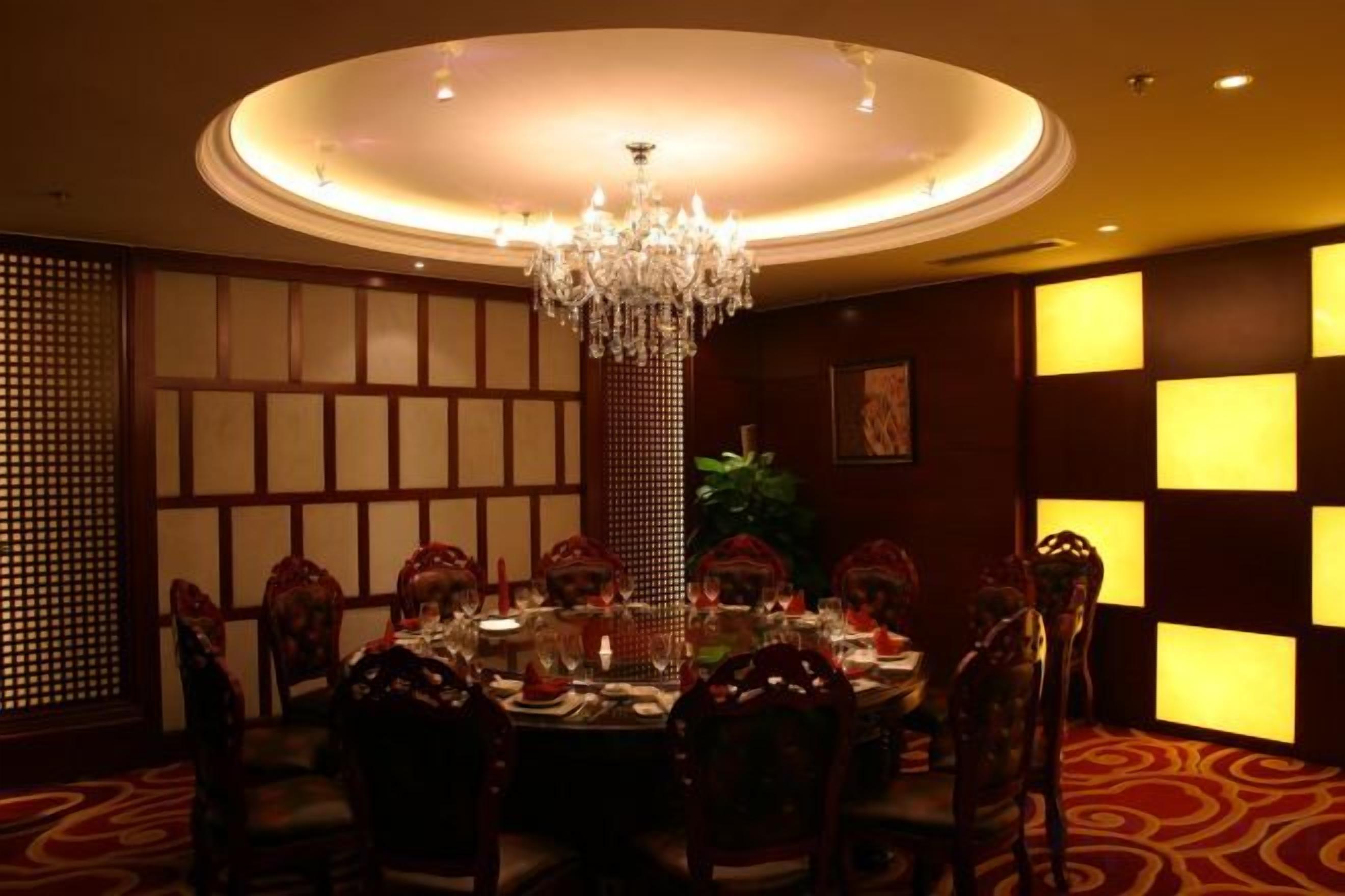 A dining area with a round table, chairs, a chandelier, and illuminated wall panels.