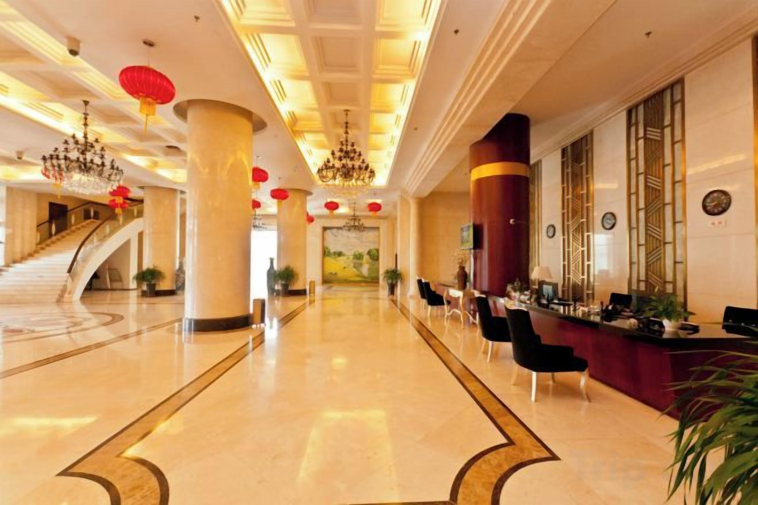 A hotel lobby with a marble floor, a reception desk, and a staircase.