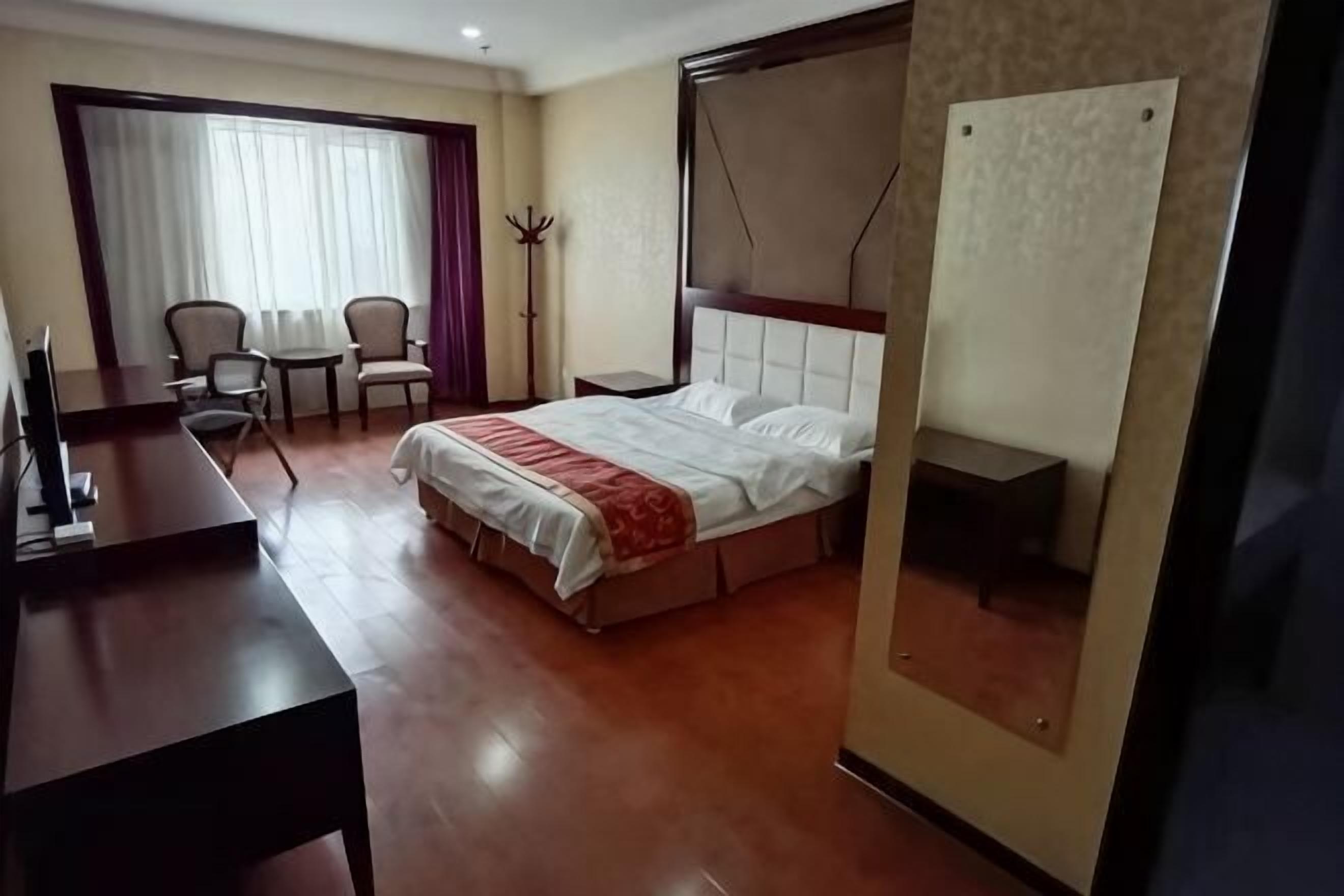 A hotel room with a bed, a desk, a chair, and a window with curtains.