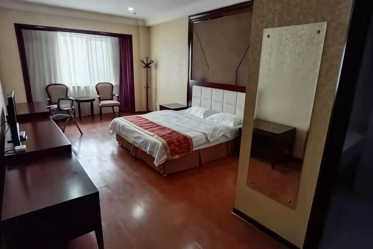 A hotel room with a bed, a desk, a chair, and a window with curtains.