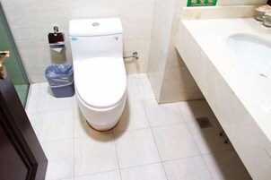 Un baño con inodoro blanco, un bote de basura y un lavabo.