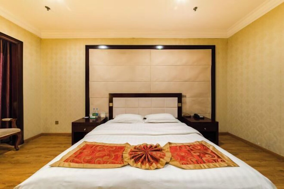 A hotel room with a large bed, a nightstand, a chair, and a wooden floor.
