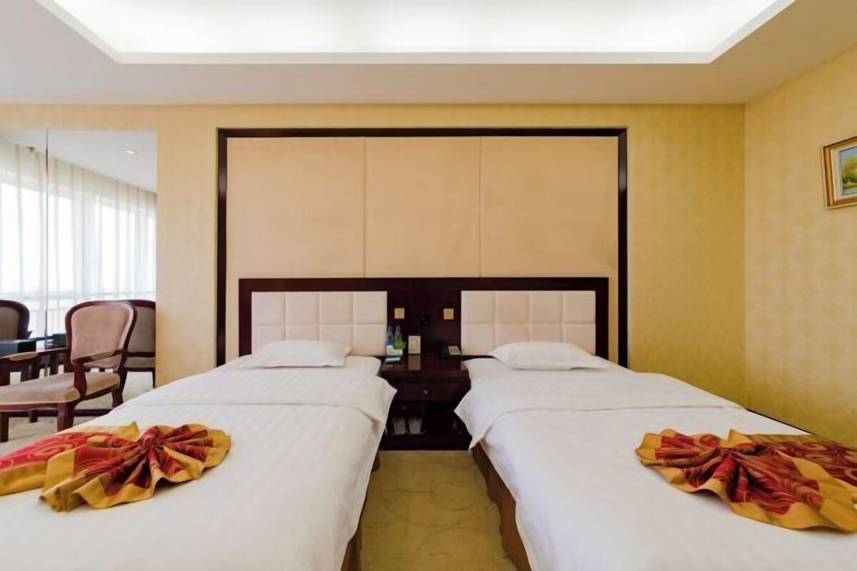 A hotel room with two beds, a nightstand, a chair, and a desk.