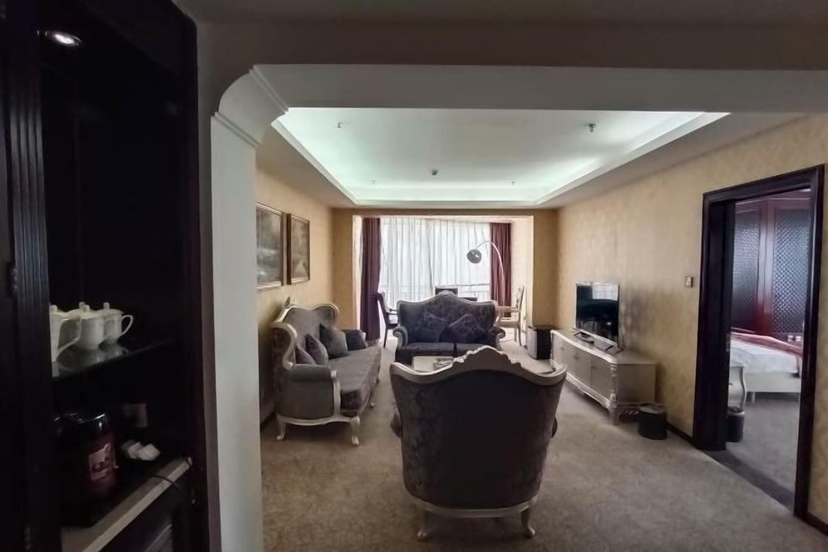 A hotel room with a sofa, armchair, TV, and a small table.