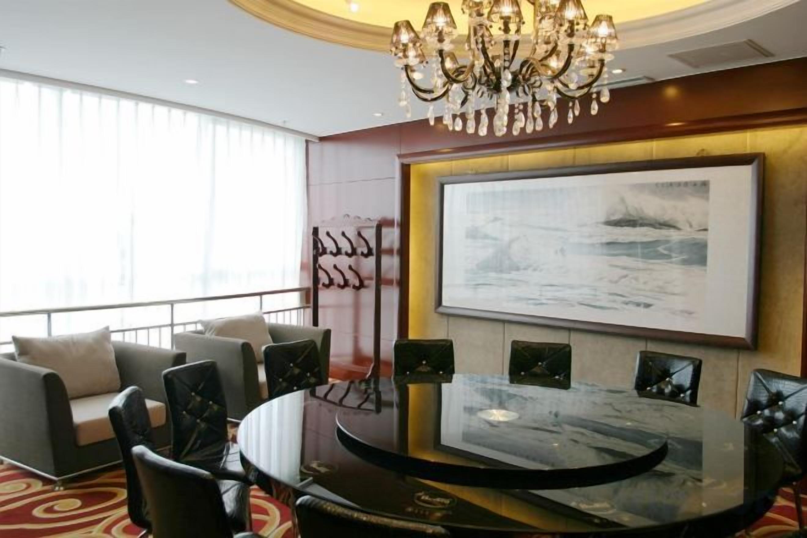 Habitación de hotel con una mesa redonda, sillas, una araña, un cuadro grande y vistas a la ciudad.