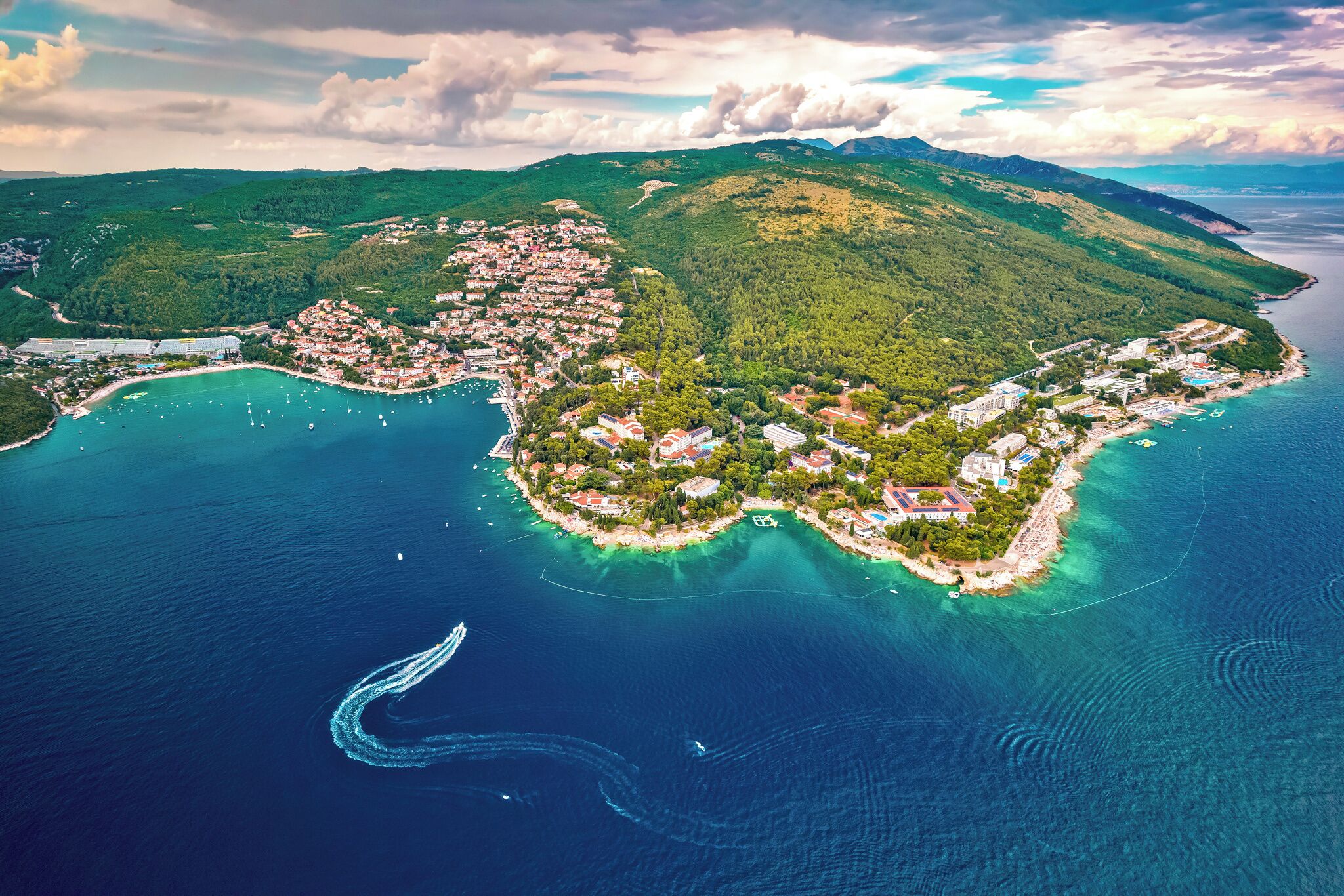 Une vue aérienne d’une ville côtière, avec un ensemble de bâtiments concentrés au centre, entourés d’eau et reliés à la terre ferme par une étroite bande de terre.