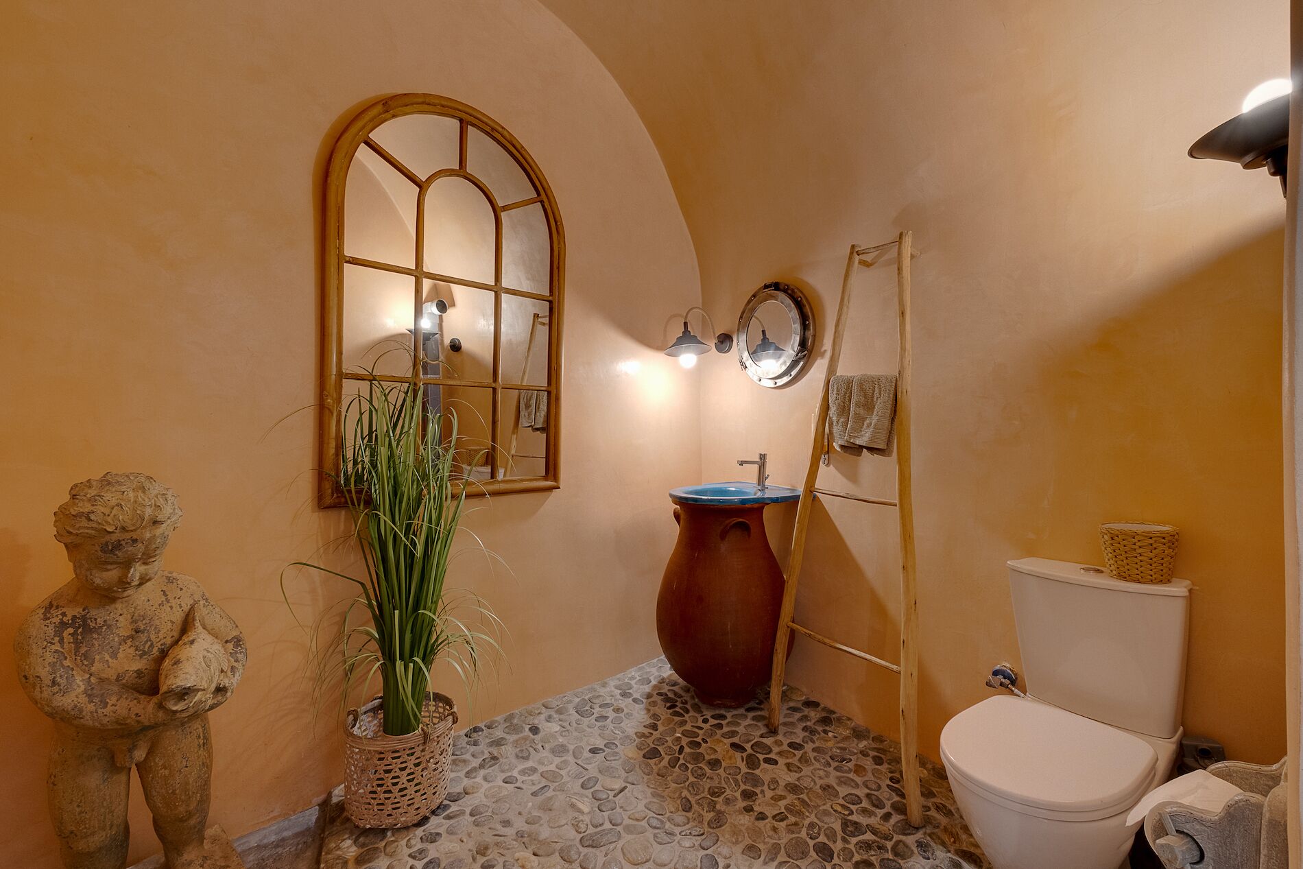 Een badkamer met een stenen vloer, een houten wastafel, een toilet en een standbeeld.