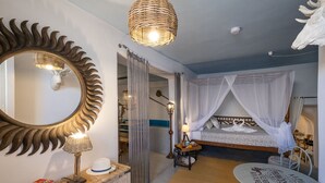 Un dormitorio con un espejo grande, una cama con dosel, una mesita pequeña y una lámpara de mimbre.