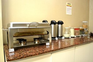 A buffet setup with a self-service station, including a coffee maker, milk jug, and various food containers. - Domus Hotel Veneza (Ipatinga)