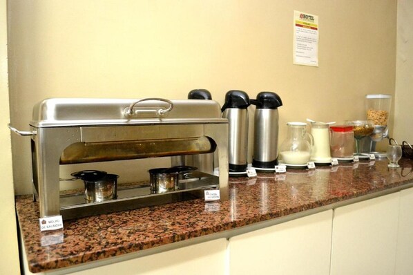 A buffet setup with a self-service station, including a coffee maker, milk jug, and various food containers. - Domus Hotel Veneza (Ipatinga)