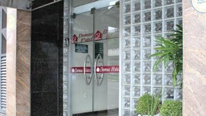 A hotel entrance with a glass door, a red mat, and a stone planter with plants. - Domus Hotel Veneza (Ipatinga)
