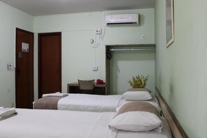 A hotel room with two beds, a desk, an air conditioning unit, and a wall-mounted shelf. - Domus Hotel Veneza (Ipatinga)