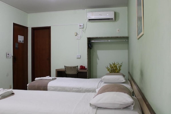A hotel room with two beds, a desk, an air conditioning unit, and a wall-mounted shelf.