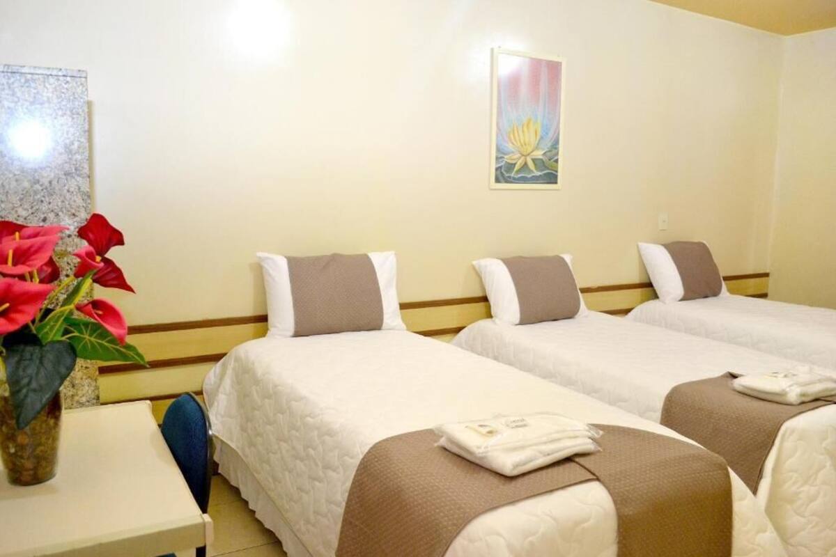 A hotel room with three beds, a small table with a vase of flowers, and a wall-mounted painting.