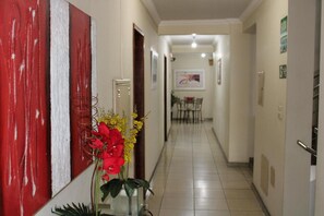 A hallway with a red wall, a door, a plant with red and yellow flowers, and a dining area in the background. - Domus Hotel Veneza (Ipatinga)