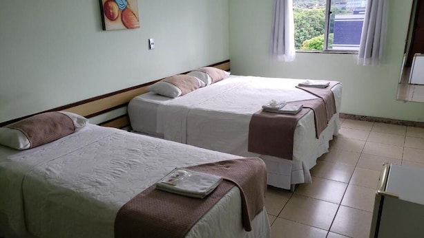 A hotel room with two beds, a window with a view, and a painting on the wall. - Domus Hotel Veneza (Ipatinga)