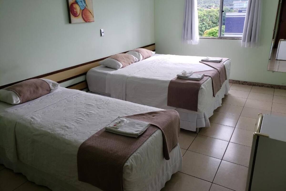 A hotel room with two beds, a window with a view, and a painting on the wall.