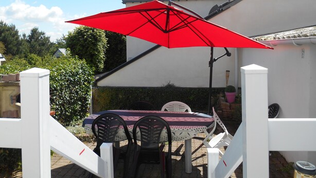 Eine Terrasse mit Tisch und Stühlen, einem roten Sonnenschirm und einem weißen Zaun.