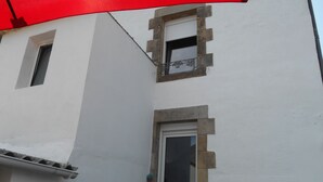 Ein weißes Gebäude mit einem kleinen Fenster und einer Tür, einem weißen Zaun und einem roten Regenschirm.