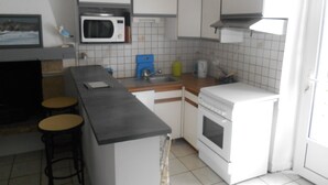 Eine kompakte Küche mit weißen Schränken, einer Mikrowelle, einem Herd und einem Spülbecken. Zwei Hocker und ein kleiner Tisch sind ebenfalls vorhanden.
