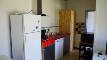 A compact kitchen with a white refrigerator, a red countertop, a sink, and a microwave.