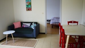 Ein Zimmer mit einem dunkelblauen Sofa, einem kleinen runden Tisch und einem Esstisch mit roten Stühlen.