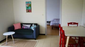 A room with a dark blue sofa, a small round table, and a dining table with red chairs.