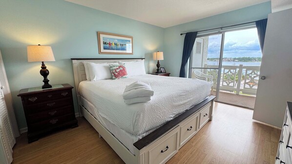 A bedroom with a bed, two bedside tables, a nightstand, a window with a view, and a balcony.