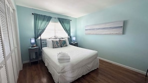 A bedroom with a bed, two bedside tables, a nightstand, a window with curtains, and a wall-mounted painting.