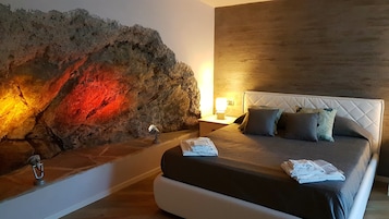 Quarto com uma grande parede de pedra, um painel de cabeceira branco e uma mesa de cabeceira com abajur.