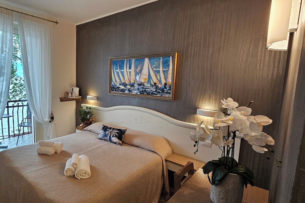 A hotel room with a bed, two bedside tables, a painting, and a potted orchid.