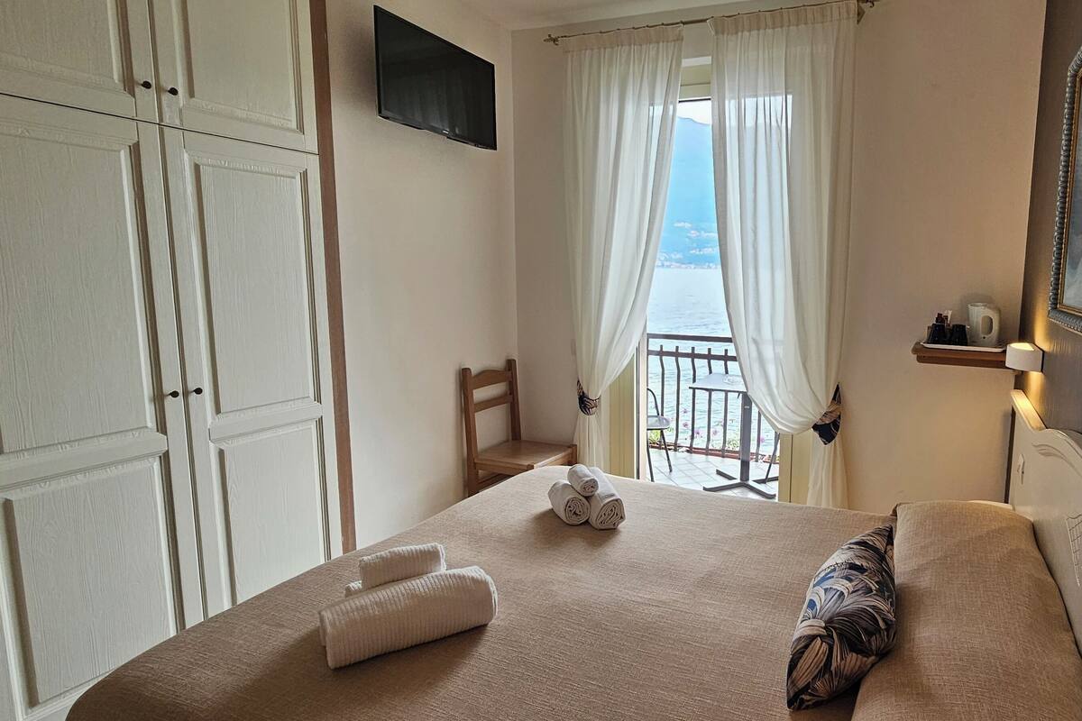 A bedroom with a bed, a chair, a TV, a painting, and a view of the sea.