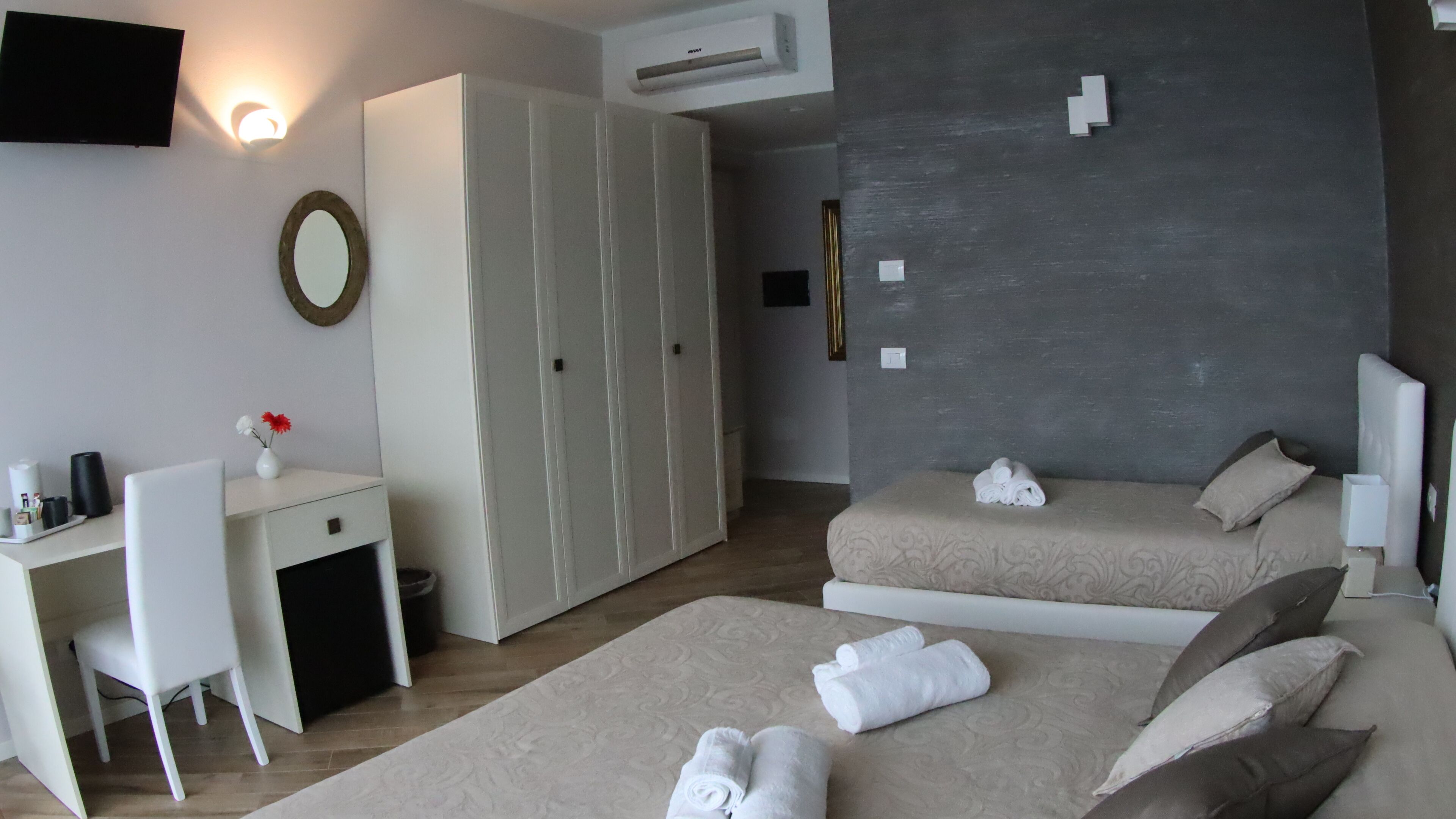 Une chambre d’hôtel avec deux lits, un bureau, une chaise, une armoire et un téléviseur fixé au mur.
