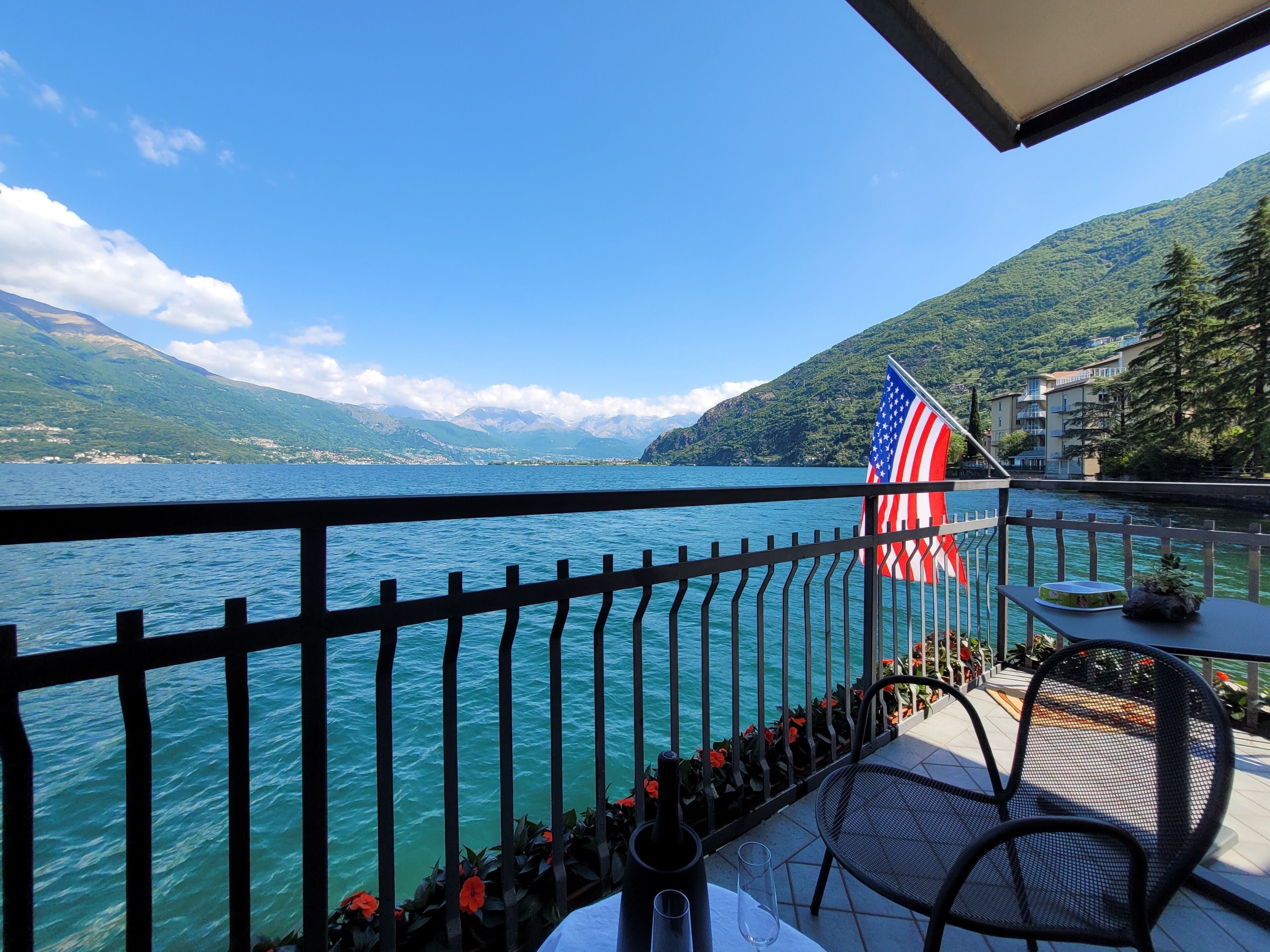 A balcony with a view of a lake, an American flag, and a table with a bottle and glass.