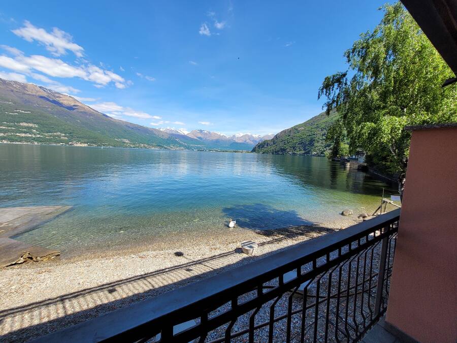 A lakeside view with clear water, a pebbled shore, and mountains in the background.